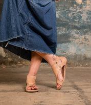 Wearing the Bed|Stü Soto tan cutout leather sandals with a cushioned footbed and a frayed denim skirt, this person stands on a concrete floor, one foot raised to reveal a tattoo on their left ankle—an effortlessly stylish look for everyday adventures.