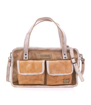 The “Stuffy” handbag by Bed|Stü is crafted in tan leather with a structured silhouette, featuring two front pockets, dual top handles, a removable shoulder strap, decorative stitching, and branded labels displayed on the front for a preppy look.