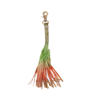 The Bed|Stü Tassel Clip features a leather keychain charm with a brass clasp and a fringed tassel in green, orange, and tan—perfect as a stylish bag accessory or leather tassel clip.