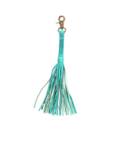 The Bed|Stü Tassel Clip features a teal leather design with multiple fringe strands and a gold clasp, making it a stylish accessory for your bag or a charming keychain. Shown against a white background.