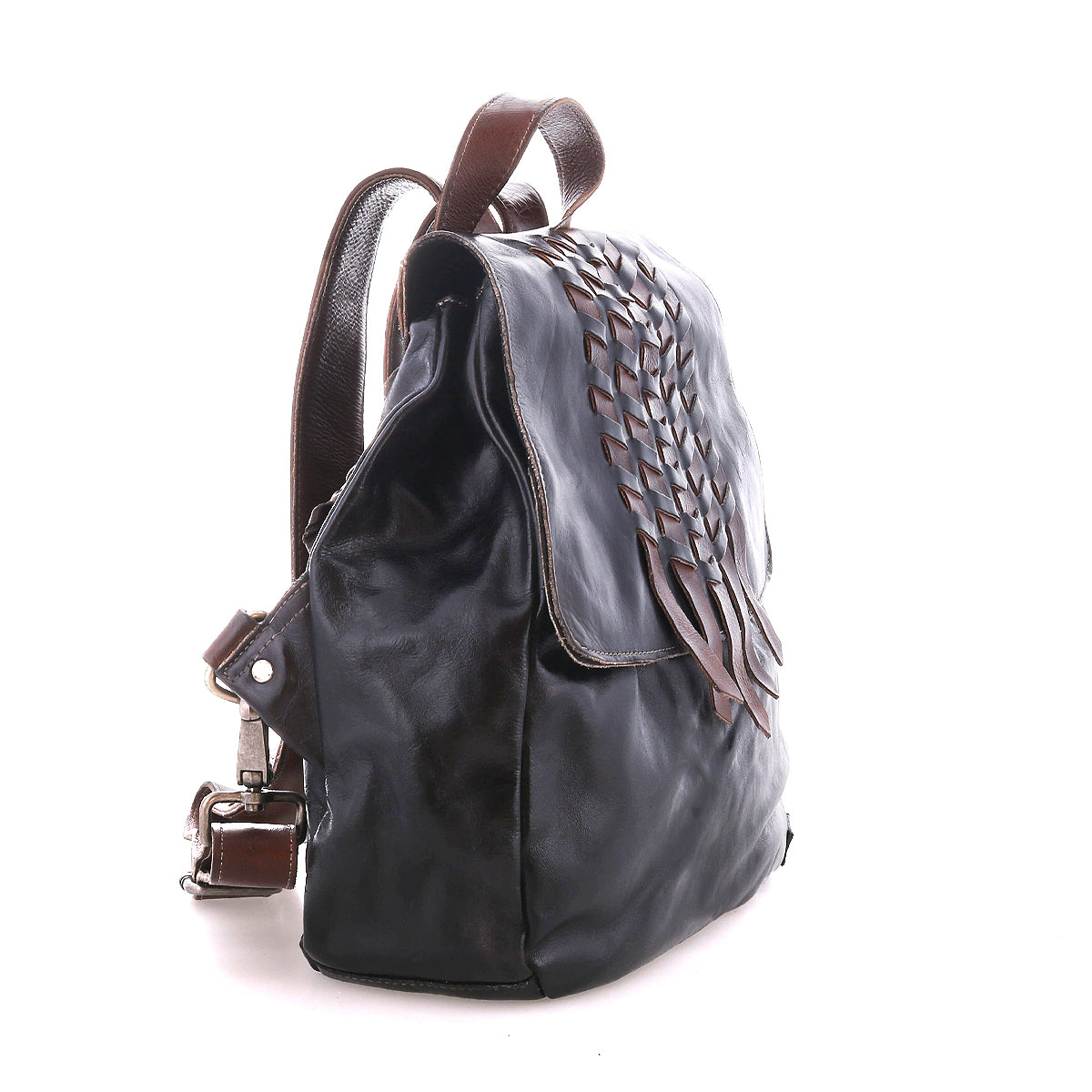 The Bed|Stü Teji backpack features a dark leather body with a handwoven flap design, brown straps, and metal hardware, shown against a white background.