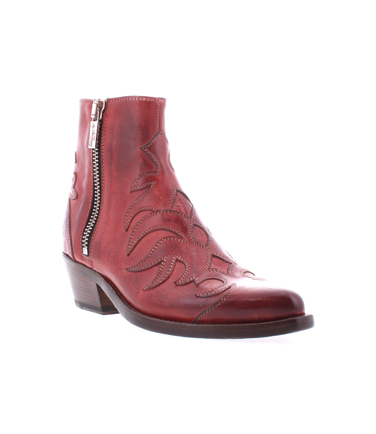The Tentativa boot by Bed|Stü is a handcrafted Italian red leather ankle boot featuring a side zipper, decorative stitching, stacked heel, and slightly pointed toe, evoking vintage Western charm. It is displayed on a white background.