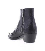The Bed|Stü Tentativa is a black leather ankle boot with a handcrafted Italian-inspired design, featuring a side zipper, low stacked heel, and decorative stitching. It is shown from the back and slightly to the side against a white background.