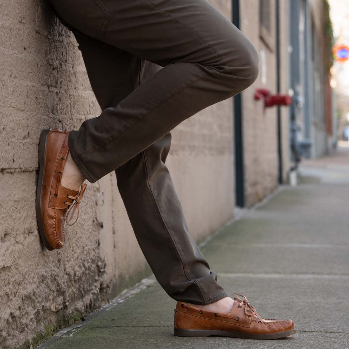 Wearing the Bed|Stü Uncle Floyd in brown, a person leans against a concrete wall on a city sidewalk, one foot casually crossed over the other.