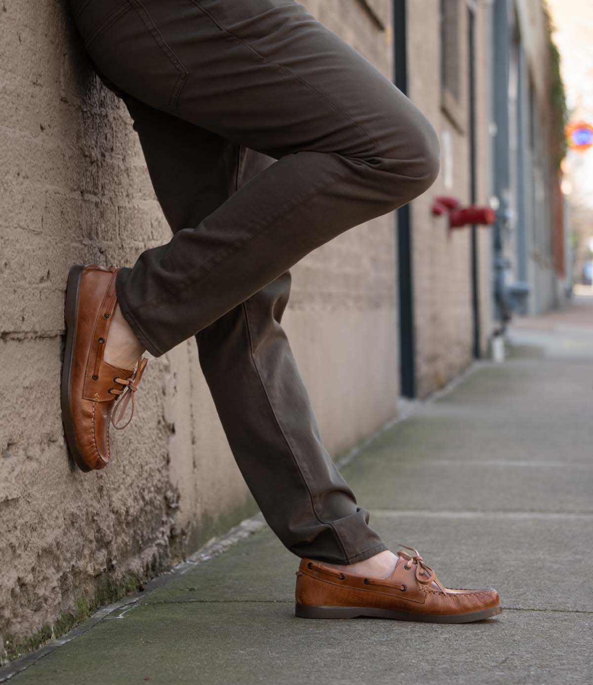 Wearing the Bed|Stü Uncle Floyd in brown, a person leans against a concrete wall on a city sidewalk, one foot casually crossed over the other.