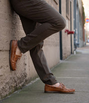 Wearing the Bed|Stü Uncle Floyd in brown, a person leans against a concrete wall on a city sidewalk, one foot casually crossed over the other.