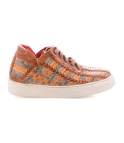 The Unwavering sneaker by Bed|Stü is a handwoven leather design in tan and gray, featuring a white sole, brown laces, and a striking red interior. Shown in profile against a white background, its dimensional woven pattern brings unique character to these comfortable sneakers.