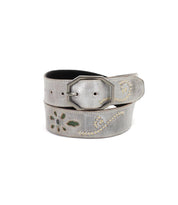 The Bed|Stü Upswing II is a handcrafted leather belt featuring decorative cutout patterns, contrast stitching, and a metal buckle, elegantly coiled against a white background. This artisanal accessory showcases subtle gray tones and intricate detailing for a sophisticated finishing touch.