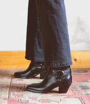Wearing Bed|Stü's Vamoose black square-toe boots with silver buckle details and black pants, the person stands on a patterned rug.