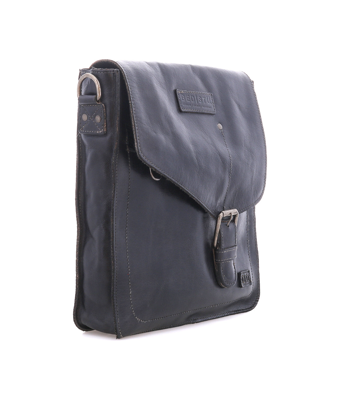The Bed|Stü Venice Beach is a black full-grain leather shoulder bag with a flap cover, buckle clasp, and visible stitching, featuring an adjustable strap for versatile crossbody wear—photographed against a white background.