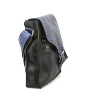 A side view of the Bed|Stü "Venice Beach" crossbody bag, crafted from black full-grain leather with a blue flap, metal buckles, and an adjustable shoulder strap.