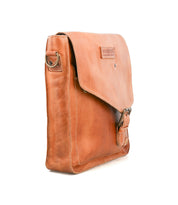 The Bed|Stü Venice Beach messenger bag, crafted from brown full-grain leather, features a front flap with buckle closure, an adjustable strap, and a side metal ring, all showcased against a white background.