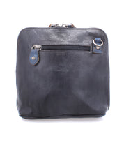 The Bed|Stü Ventura is a square-shaped black leather crossbody bag with a lightweight design, featuring an exterior zip pocket, silver zipper pull, and a small metal ring near the top right corner, shown against a white background.