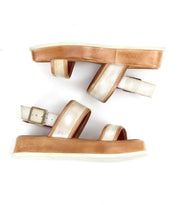 A side view of the Bed|Stü Vice sandals is shown on a white background, featuring strappy metallic gold straps, tan platform soles, and an adjustable ankle strap.
