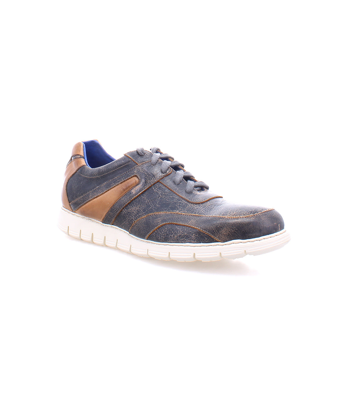 The Bed|Stü Wardell sneaker features dark blue and brown layered leather, contrasting stitching, blue laces, and a white cushioned sole that adds a modern edge. Displayed against a white background.