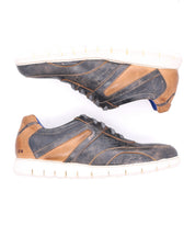Experience the modern edge of Bed|Stü's Wardell sneakers—casual, layered leather shoes featuring distressed blue and tan uppers, white cushioned soles, and blue accents, shown side by side on a white background.