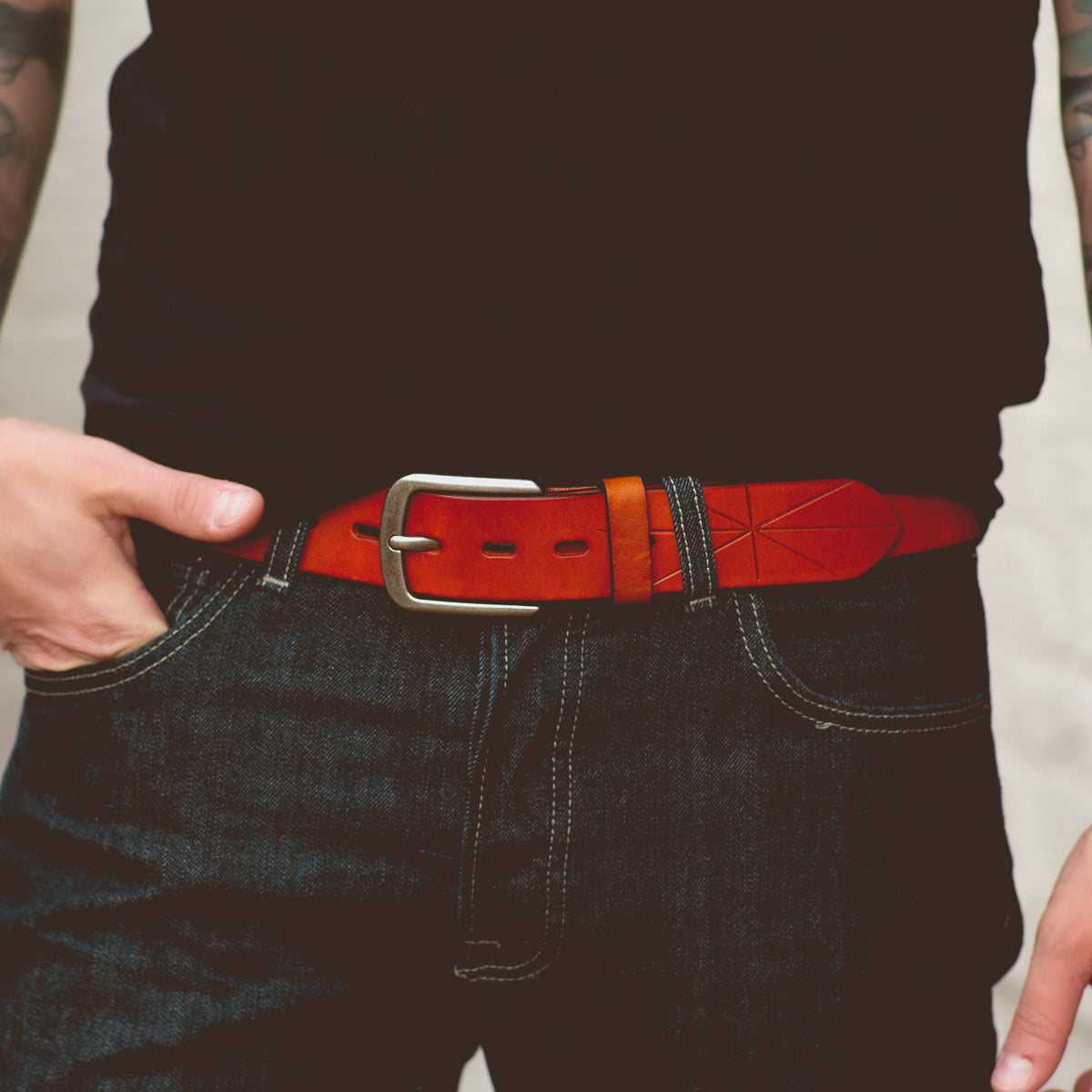 A person wearing dark jeans and a black shirt with the Bed|Stü Westham belt—a bright brown leather belt featuring a stamped star design and a silver, removable buckle—stands with one hand resting on the belt.