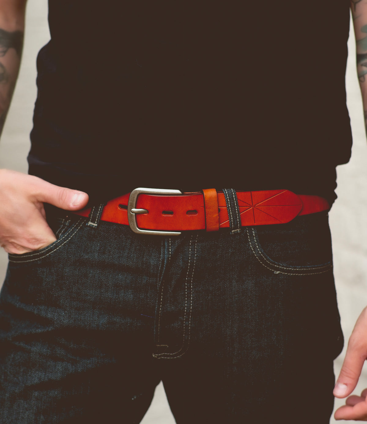 A person wearing dark jeans and a black shirt with the Bed|Stü Westham belt—a bright brown leather belt featuring a stamped star design and a silver, removable buckle—stands with one hand resting on the belt.