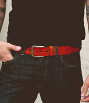 A person wearing dark jeans and a black shirt with the Bed|Stü Westham belt—a bright brown leather belt featuring a stamped star design and a silver, removable buckle—stands with one hand resting on the belt.