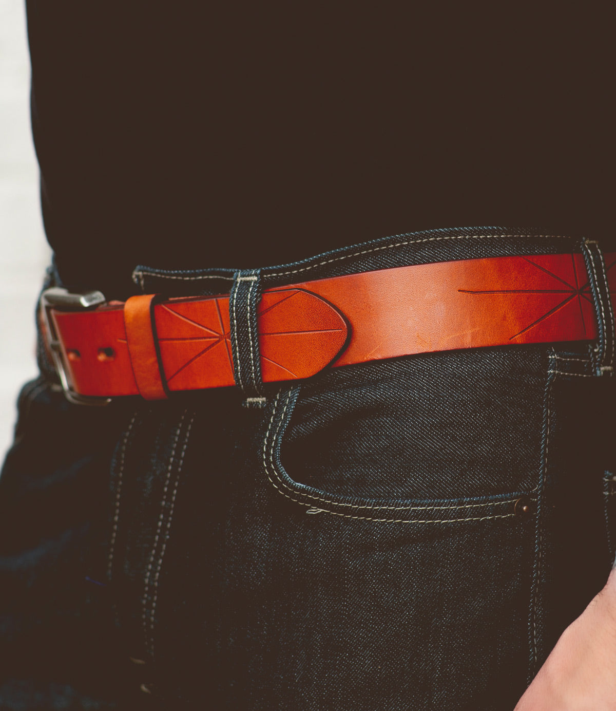 A person wearing blue jeans and a black shirt with the Bed|Stü Westham brown leather belt, which features decorative stitching and a removable buckle.