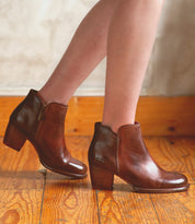 Wearing Bed|Stü’s Yell handmade leather ankle boots with side zippers and medium heels, a person stands on a wooden floor against a light-colored wall.