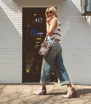 A woman wearing a striped sleeveless top, jeans, and Bed|Stü Yell high-heeled leather boots walks along the sidewalk in front of a white brick building with a glass door labeled "Vancel.