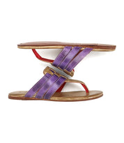 Two Yoli sandals by Bed|Stü, featuring brown soles and purple woven uppers, are positioned upright and balanced sole-to-sole, forming an S-shape against a white background. Designed with a cushioned insole for added comfort, these sandals combine stylish detailing with everyday wearability.