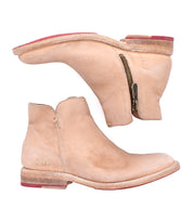 A pair of tan Yurisa handcrafted ankle boots by Bed|Stü, featuring side zippers and red-accented leather outsoles, shown from a side and bottom angle.