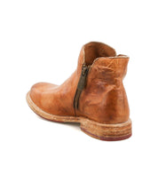 Introducing the Yurisa by Bed|Stü: a tan leather ankle boot featuring a side zipper, worn texture, and a stacked wooden heel. Viewed from the back and slightly to the side, this handcrafted boot showcases its durable leather outsole, blending lasting comfort with distinctive style.