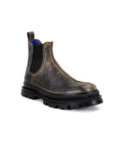 The Bed|Stü Accelerate boot, a single brown distressed leather Chelsea style, features black elastic side panels, a blue pull tab, and a chunky black lug outsole for a modern edge, shown against a white background.