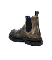 The Bed|Stü Accelerate boot features brown leather with black elastic side panels, a blue pull tab, and a thick black lug outsole for a modern edge, shown angled from the back.