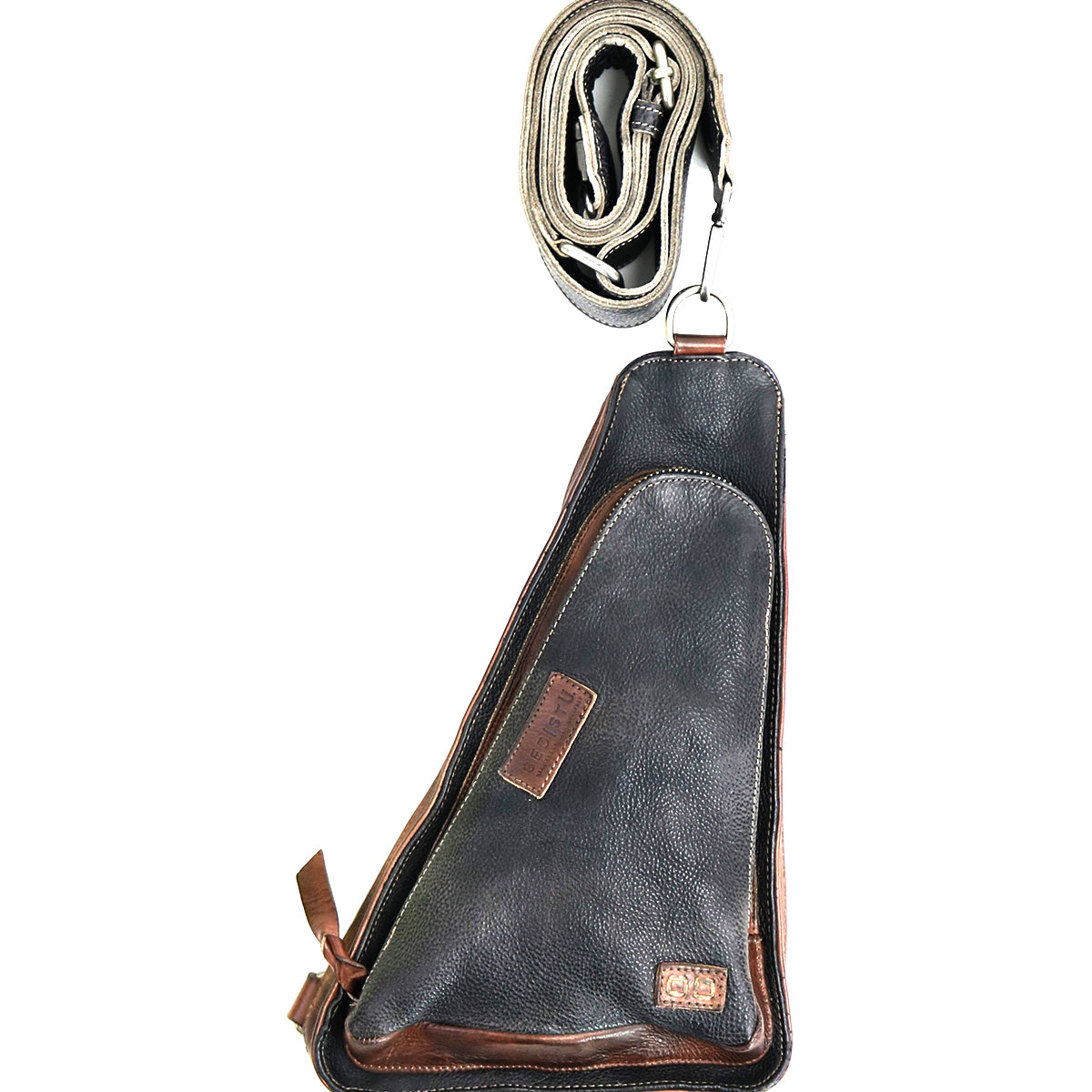 The Bed|Stü Adept is a black and brown compact sling bag crafted from vegetable-tanned leather, featuring a zippered front pocket. It is displayed with its matching adjustable strap rolled up above it.