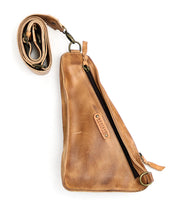 Introducing the Adept by Bed|Stü—a compact sling bag meticulously crafted from premium vegetable-tanned leather in a rich tan hue. It features a long, adjustable strap for versatile wear, a prominent zipper pocket, and a small branded Bed|Stü label on the front.