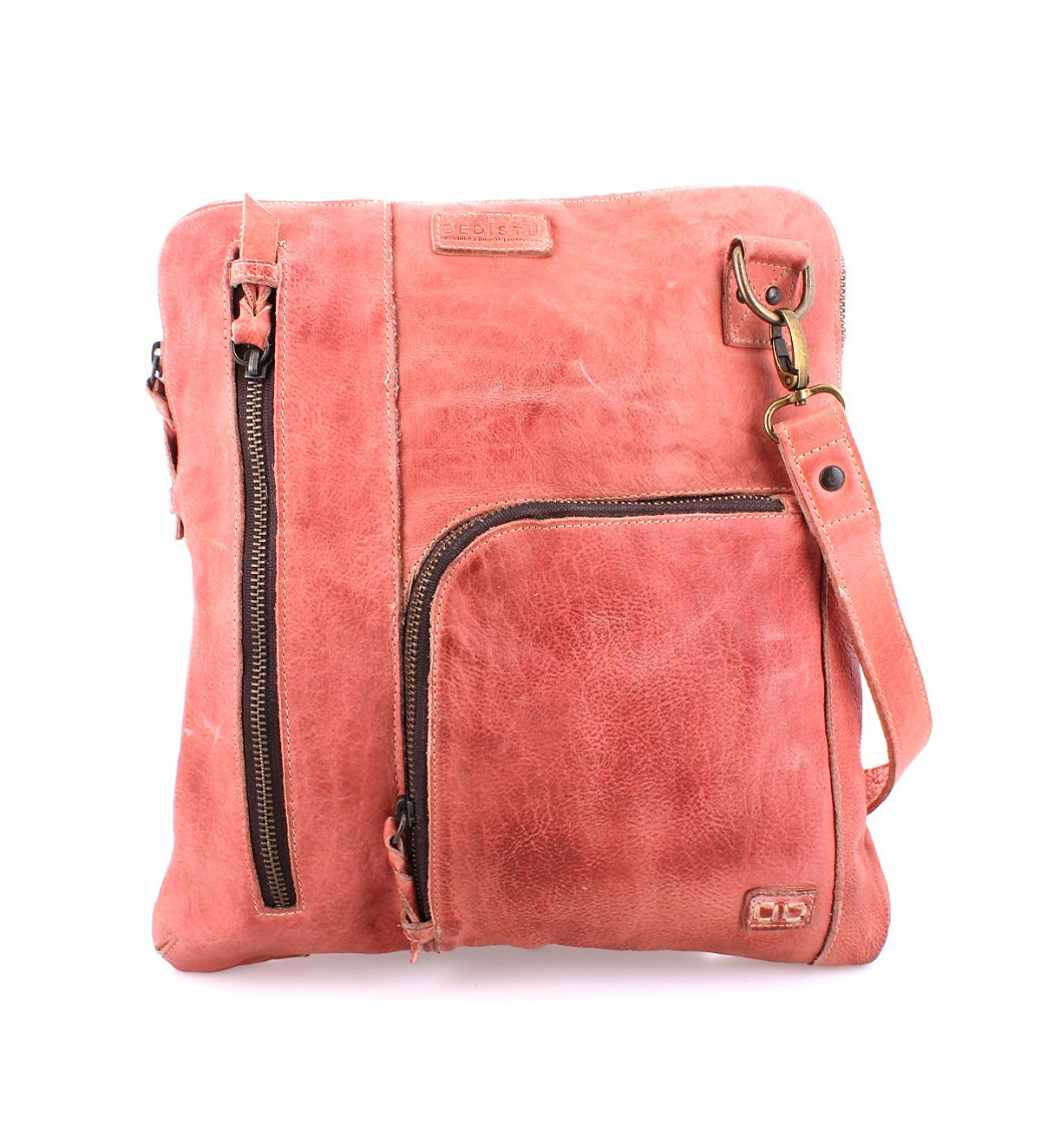 The Bed|Stü Aiken is a square-shaped crossbody bag crafted from distressed pink full-grain leather, featuring brass hardware, multiple zippered pockets, anti-theft security features, and an adjustable shoulder strap.