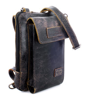The Bed|Stü Alelike is a small, dark brown weathered leather crossbody bag featuring a front flap, zipper compartment, and adjustable strap—an ideal compact purse for keeping your travel essentials organized and close at hand.