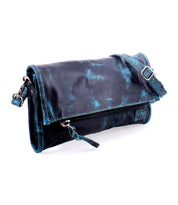 The Bed|Stü Amina is a black leather clutch featuring blue distressed accents, a front zipper, and an adjustable crossbody shoulder strap, shown on a white background.