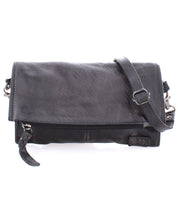 The Bed|Stü Amina is a black leather crossbody bag featuring a fold-over flap, front zipper, and adjustable shoulder strap—perfect for carrying your essentials as a stylish crossbody or a sleek clutch.