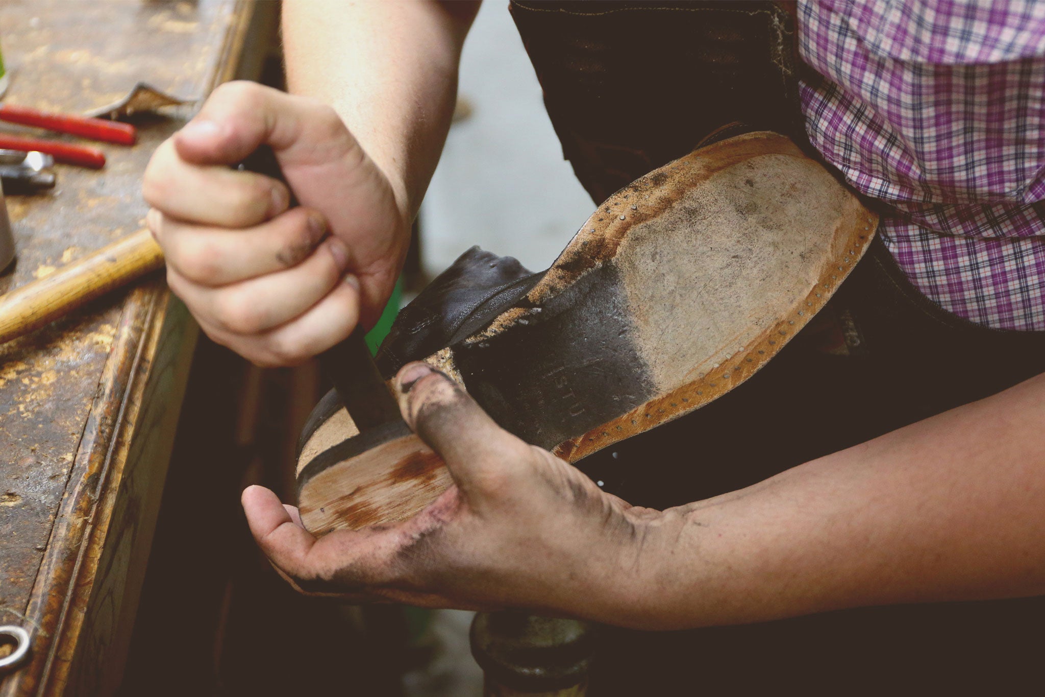 Craftsperson repairing a black leather shoe by hand with tools at a workbench.