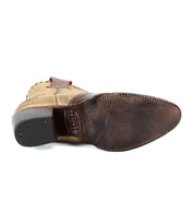 The Bed|Stü Baila II is a tan, western-style boot shown from the bottom, featuring a pointed toe silhouette. Its dark brown leather sole displays visible stitching and metal details near the heel, showcasing artisanal construction.