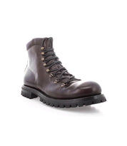 The Bed|Stü Barge is a dark brown lace-up combat boot crafted from Italian leather, featuring metal eyelets and a thick black treaded sole, shown angled to display the front and side against a white background.