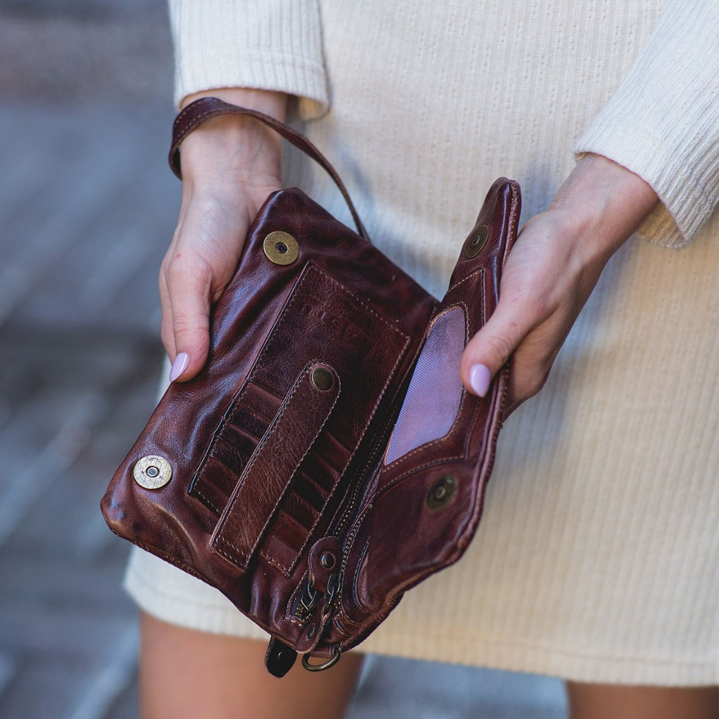 A person in a cream dress holds an open Bed|Stü Bayshore wallet—crafted in brown leather—with multiple empty compartments visible.