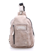Beau by Bed|Stü is a beige leather sling bag featuring a front zippered pocket, stitched logo patch, top handle, and adjustable shoulder strap—perfect as a stylish and compact backpack for your everyday essentials.