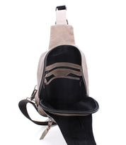 The Beau by Bed|Stü is a beige leather sling bag with a black interior, shown open to reveal both zippered and slip pockets. This compact backpack features a single adjustable strap and silver zipper hardware.