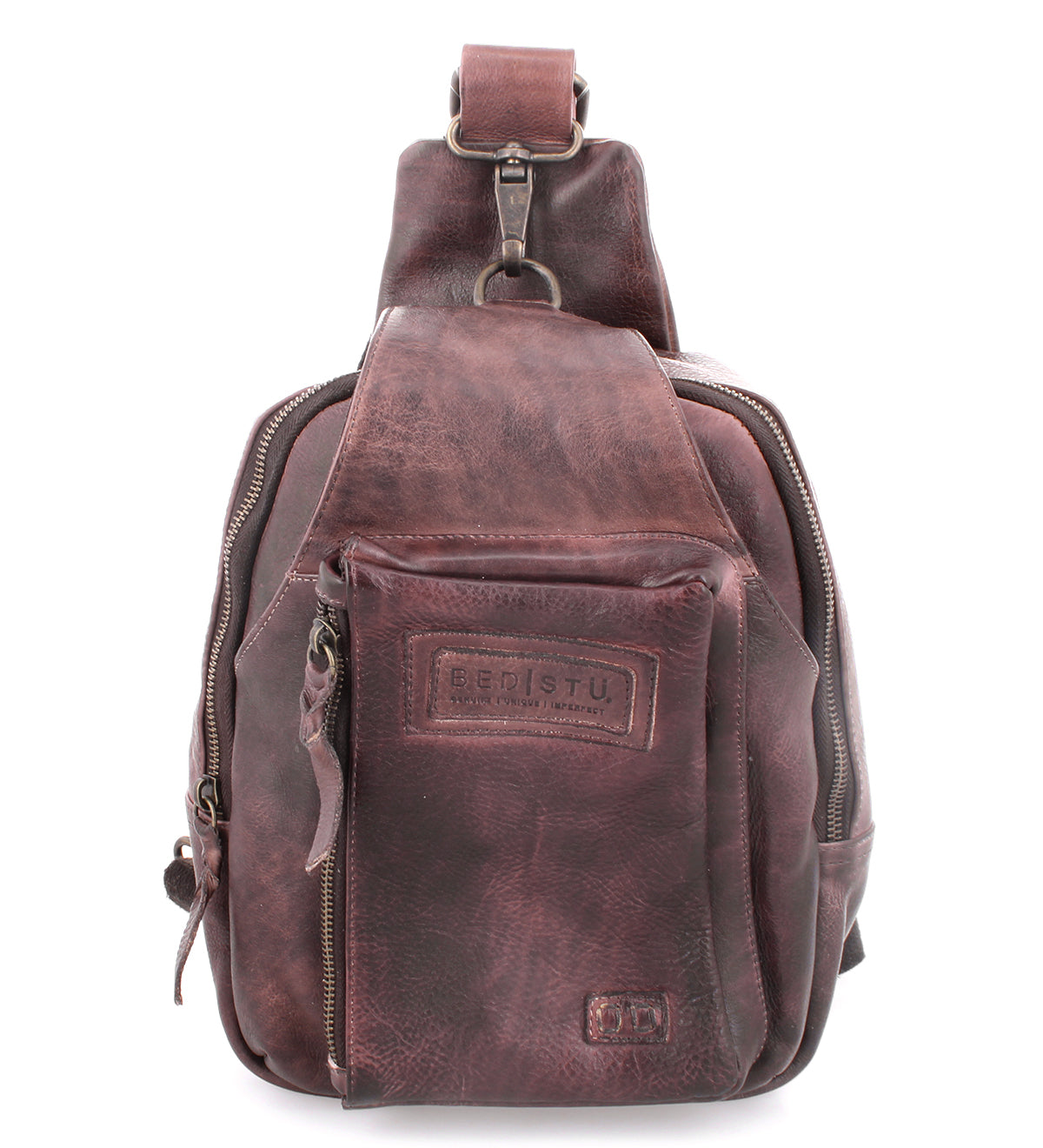 The Beau backpack by Bed|Stü is a compact brown leather sling bag featuring a front zipper pocket, side pocket, and a single adjustable shoulder strap. It showcases visible stitching and is finished with a rectangular patch embossed with text.