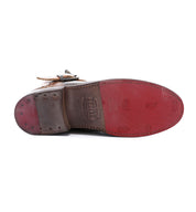 The image features the sole of the Becca by Bed|Stü, a brown leather dress shoe distinguished by its red rubber section and visible stitching, displayed sole up and showcasing durable craftsmanship similar to that of an engineer boot with a sturdy leather shaft.