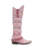 The Bed|Stü Betting is a tall pink cowboy boot featuring decorative stitching, studded harness details, and a pointed toe. Handcrafted from premium leather, it is displayed on a white background.