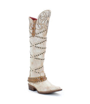 Betting by Bed|Stü: Tall white handcrafted leather boots featuring decorative stitching, floral inlays, and metal studs; designed with studded harness details and brown accents on the shaft, heel, and instep strap; completed with a low wooden heel.