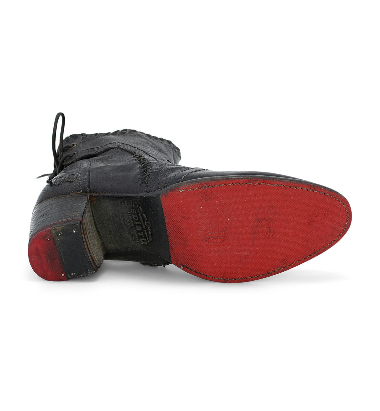 The Bia by Bed|Stü is a black leather ankle boot shown from the bottom, featuring a worn red sole, stacked heel, and visible stitching around the edge. Expertly handcrafted from vegetable-tanned leather, it offers lasting quality and unique character.
