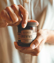 A person opens a jar labeled "Revive Leather Cream" from Bed|Stü, a premium leather conditioner, while holding it in their other hand.