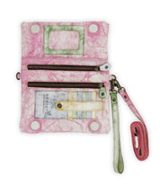 The Bed|Stü Cadence is a pink and white marbled 3-in-1 leather wallet with green and beige accents, featuring two zippered pockets, card slots, and an attached wrist strap, displayed open on a white background.